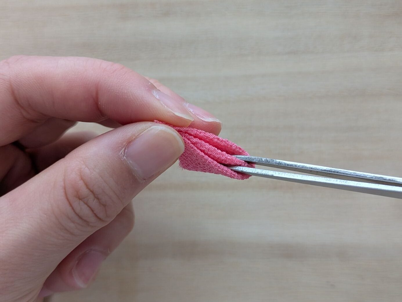 ピンクの布の花びらからピンセットを抜くところ