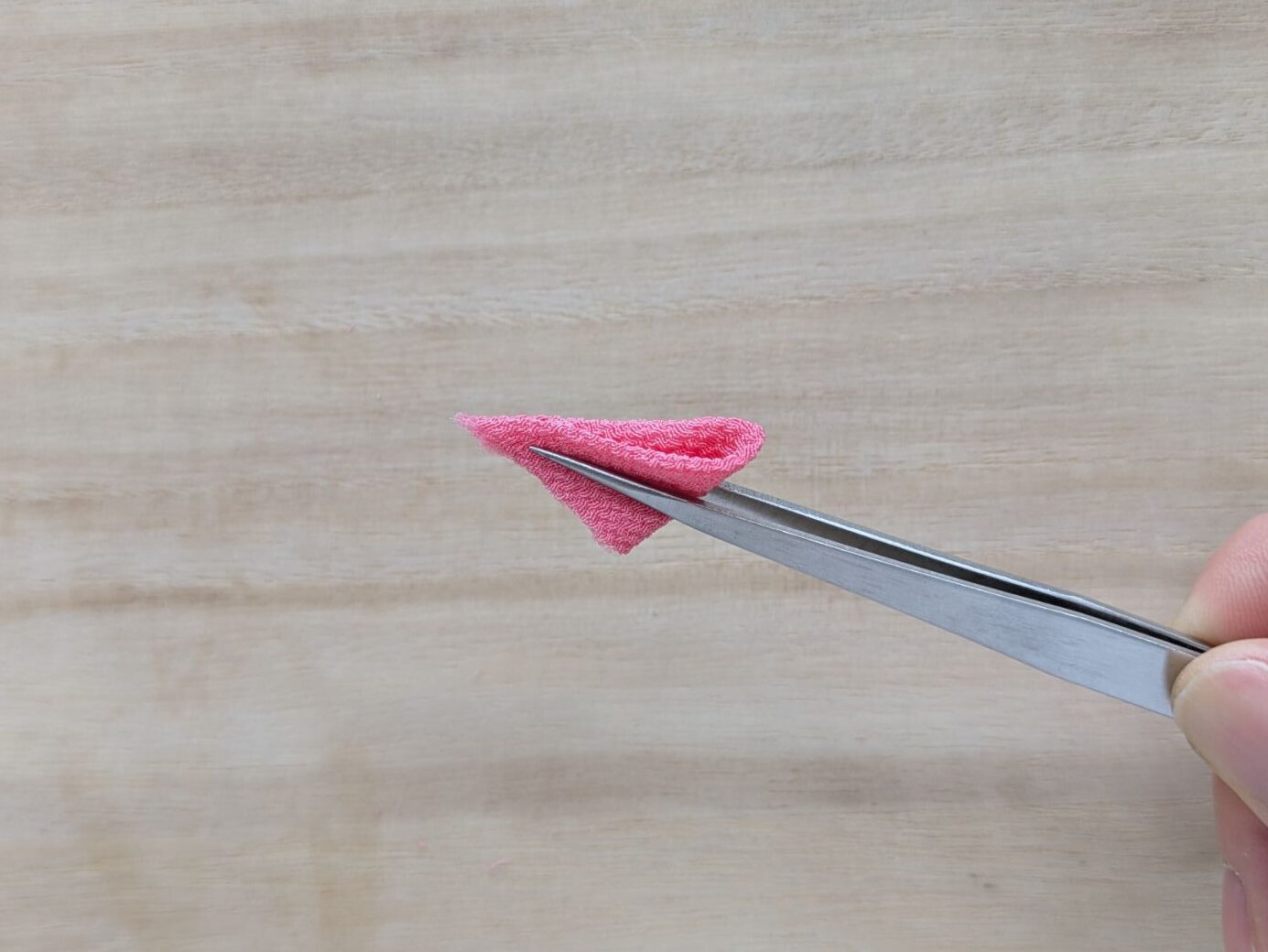 ピンクの折った花びらをピンセットで持っているとこと